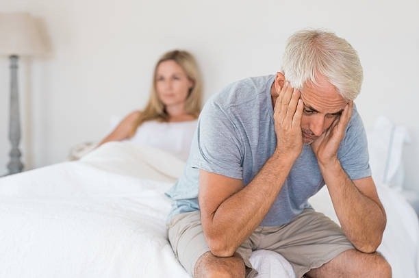 A couple sitting on a Bed, looking distressed, representing the emotional impact of sexual dysfunction