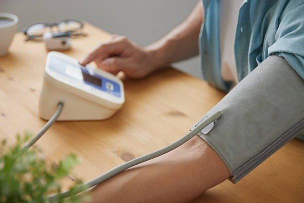 A person with hypertension measures their blood pressure at home using a digital monitor on their arm.